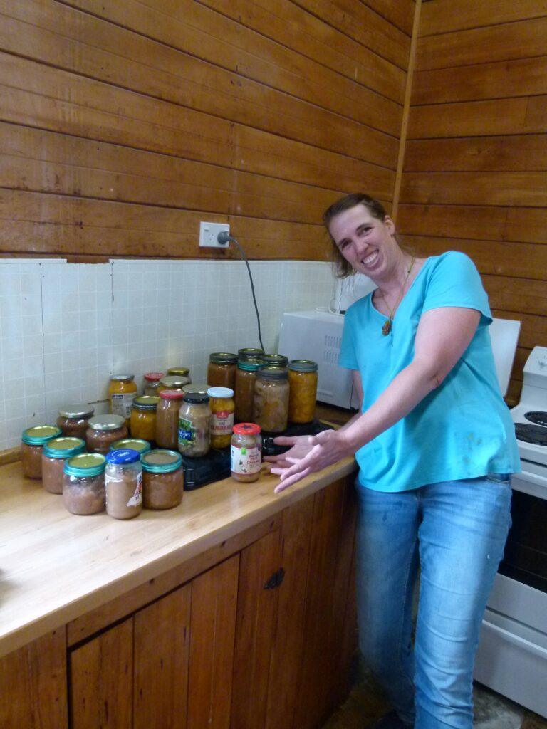 Woman smiling beside a row of homemade fruit preserves and chutneys