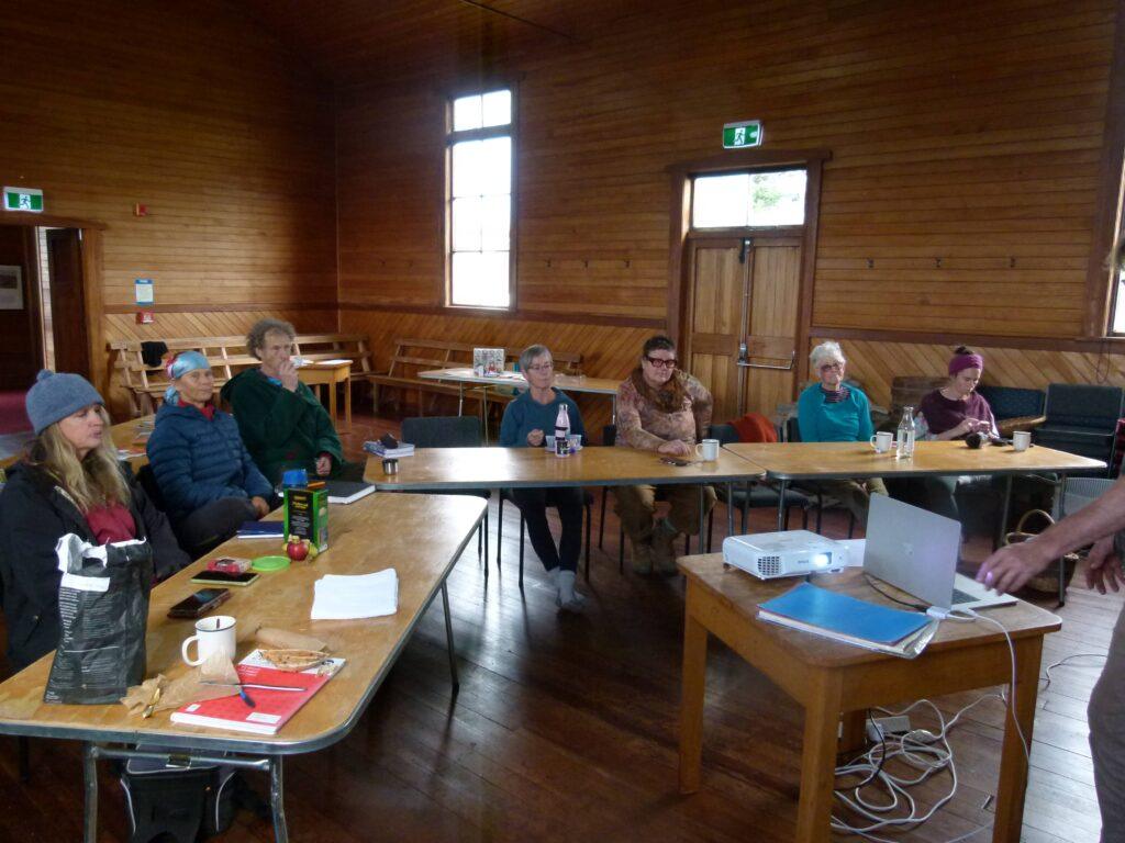 Community members seated at tables in Bainham Hall listening to a seed saving workshop presentation