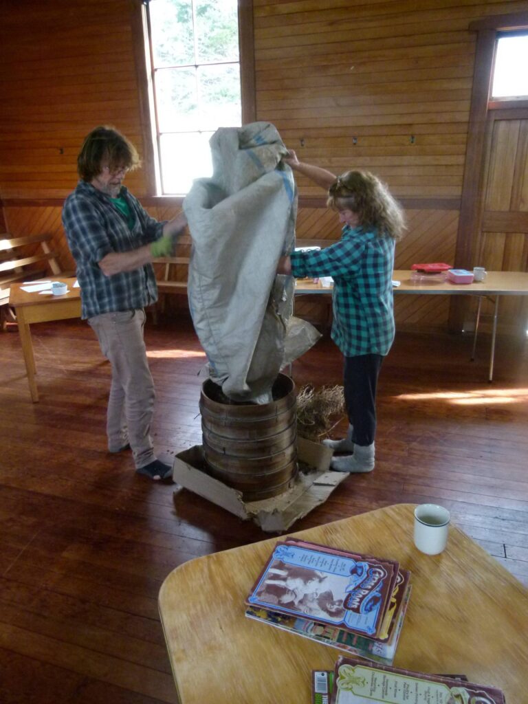 Two people threshing seeds using wooden sieves stacked on top of each other at a community seed saving workshop