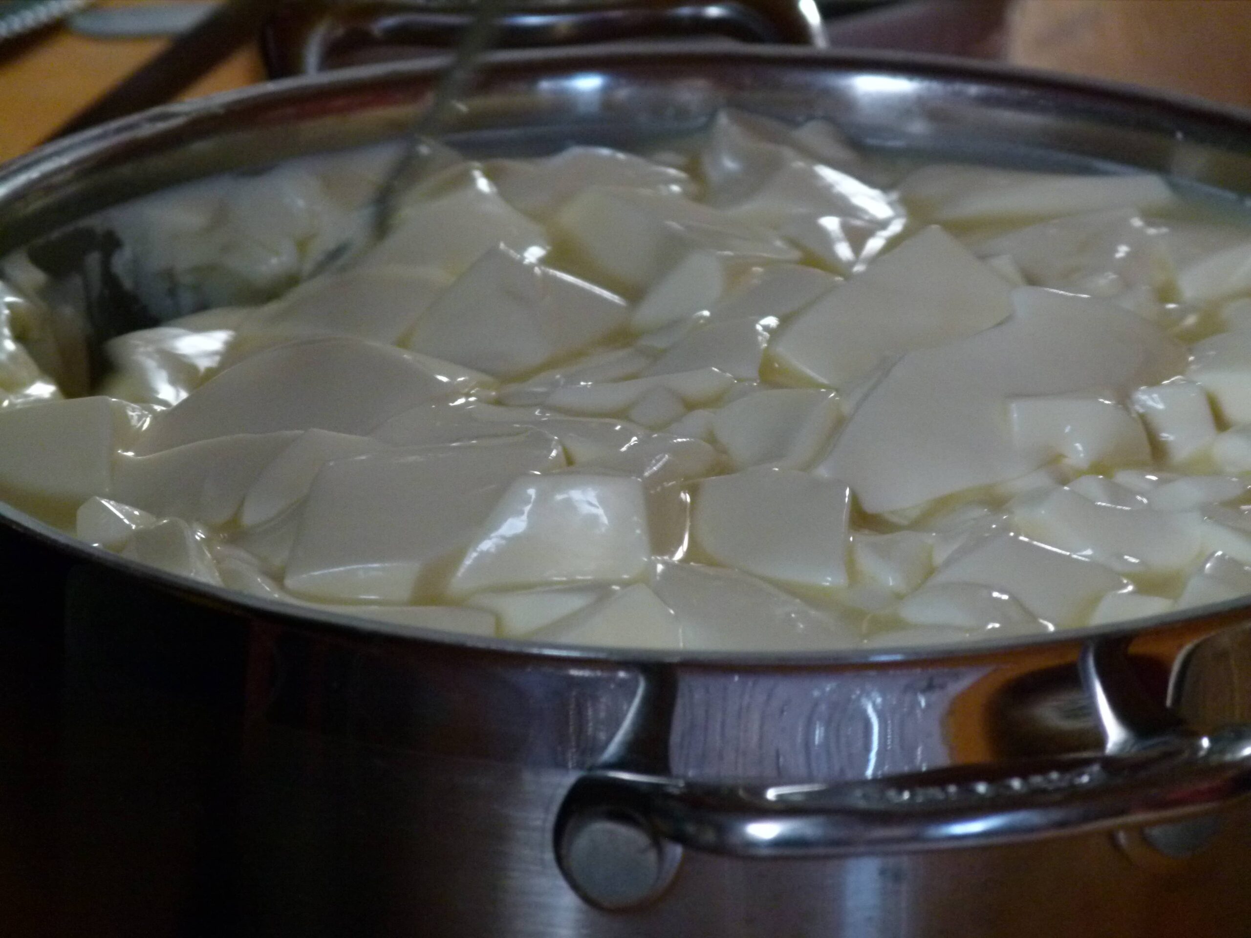 Close-up of curds floating in hot golden whey in a wide stainless steel pan