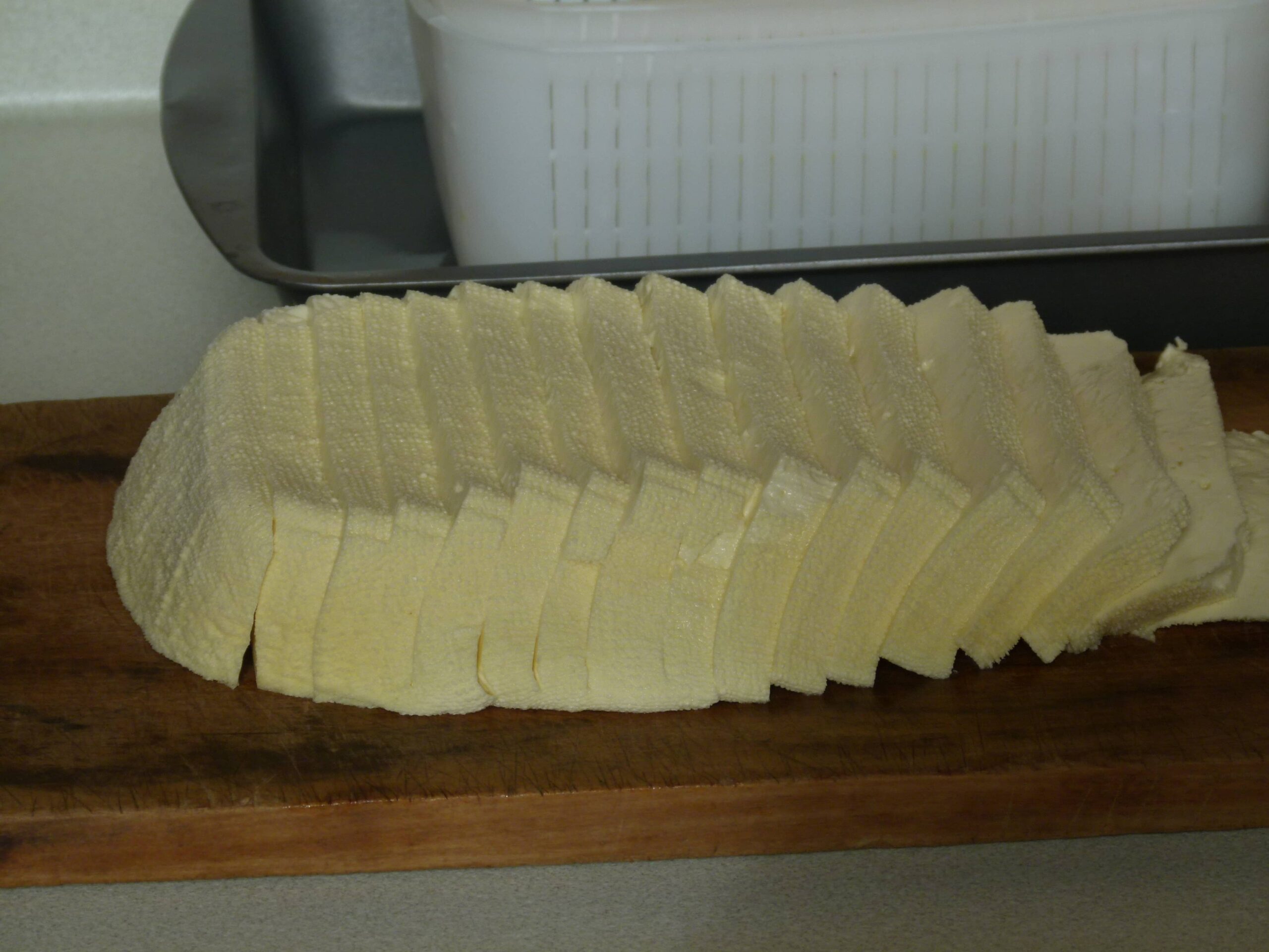 A long block of freshly made halloumi cheese sliced into even pieces and arranged on a wooden board